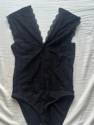 Svart spetsbody från Zara - Snygg svart body från Zara med djup V-ringning och spetsdetaljer längs kanterna. 