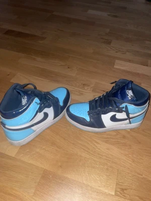 Nike Air Jordan 1 High Blue Chill UNC Patent  - Snygga Nike Air Jordan 1 Mid sneakers i blått och vitt med svarta detaljer och klassisk swoosh-logga på sidan. Skorna har högt skaft och är tillverkade i läder med perforerad tå för extra ventilation. Perfekta för dig som gillar streetwear och vill sticka ut. Priset kan diskuteras vid snabbt köp. Hör av dig vid frågor om leverans eller produkten.