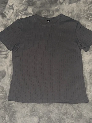 Mörkgrå ribbad t-shirt - mörkgrå t-shirt med diskret ribbad struktur och korta ärmar. Enkel och stilren modell med rund halsringning. Materialet känns mjukt och bekvämt mot huden.