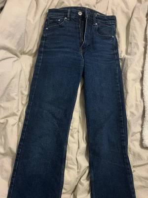 Mörkblå bootcut jeans - Snygga mörkblå bootcut jeans med klassisk femficksdesign och silverfärgade knappar. Jeansen har raka ben och är tillverkade i ett slitstarkt denimtyg som ger en cool look. Perfekta för dig som gillar en tidlös och trendig stil.