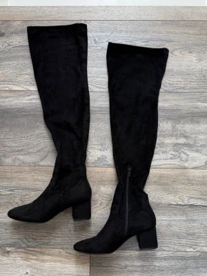 Svarta overknee stövlar med klack - Säljer ett par svarta overknee stövlar i mockaimitation med bred klack och dragkedja på insidan. Stövlarna har en stilren design och passar perfekt till höstens och vinterns outfits. Supersnygga till både kjol och jeans!
