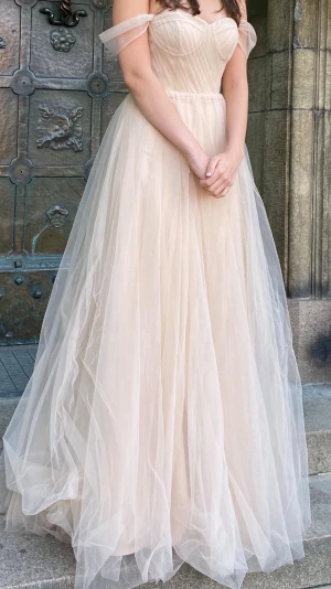 Champagnefärgad balklänning i tyll - Drömmig långklänning i champagnefärgad tyll med offshoulder-band och markerad byst. Klänningen har ett romantiskt, svepande fall och flera lager tyg som ger volym. Perfekt för bal eller speciella tillfällen. Använd på en bal, inga fläckar eller märken, som ny. Skyddspåse från dressroom  medföljer klänningen. Nypris ca4500kr