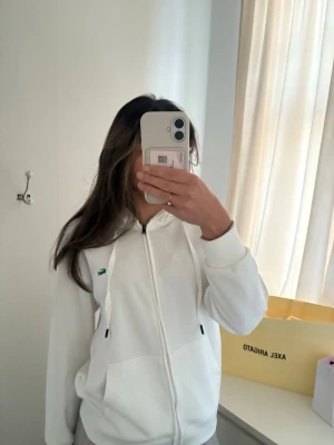 Vit zip-hoodie från Lacoste - Snygg vit hoodie med dragkedja från Lacoste. Klassisk krokodillogga på bröstet, huva med dragsko och två fickor framtill. Använd endast en gång inte riktigt min stil. I fint skick inga synliga defekter. Tröjan är unisex var igentligen köpt till min bror men va för liten för honom. Pris kan diskuteras. Nypris va ca 1800