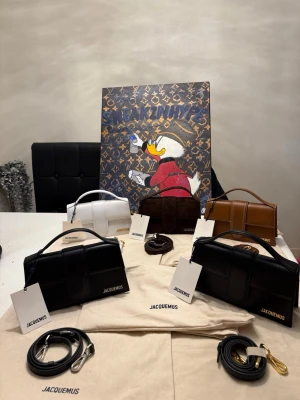 Jacquemus Le large bambino  - Snygg Jacquemus Le large bambino handväska i flera färger som svart, vitt, brunt osv. Väskan har en stilren rektangulär form, topphandtag och avtagbar axelrem i läder. Guldiga metalldetaljer och präglad Jacquemus-logga framtill. Perfekt accessoar för att lyfta din outfit. Alla är helt nya medföljer även tags & dustbag. Priset är i st pris!