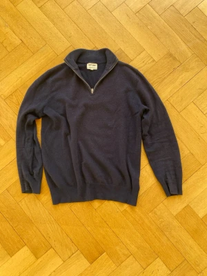 Mörkblå kashmirtröja Soft Goat - Mörkblå stickad tröja från Soft Goat i 100% kashmir. Tröjan har halv dragkedja vid kragen, ribbade muddar och en klassisk, avslappnad passform. Perfekt för dig som gillar mjuka och lyxiga material.