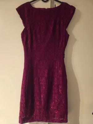Vinröd spetsklänning med capärm - Vinröd kortklänning med vackert spetsmönster och figurnära passform. Klänningen har capärm och rund halsringning, perfekt för dig som vill ha en elegant look. Dragkedja i ryggen för enkel påklädning. Står XS men skulle säga XS-S.