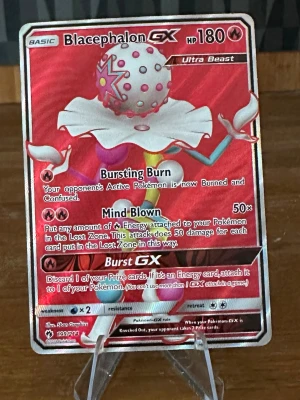 Blacephalon GX Pokémonkort - Säljer ett Blacephalon GX Ultra Beast Pokémonkort med holografisk röd finish. Kortet har 180 HP och flera kraftfulla attacker som Bursting Burn, Mind Blown och Burst GX. Perfekt för samlare och Pokémon TCG-spelare.