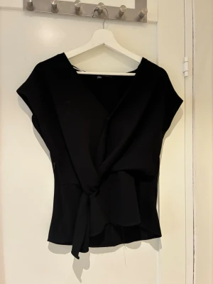 Svart omlottopp från Zara - Stilren svart omlottopp från Zara med knyt i midjan och v-ringad hals. 