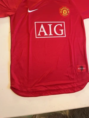 Manchester United Nike matchtröja röd - Klassisk röd Manchester United matchtröja från Nike med AIG som sponsortryck på bröstet och klubbmärke broderat på vänster sida. Tröjan har rund hals och är tillverkad i lätt, ventilerande material som passar perfekt till fotbollsträning eller match.