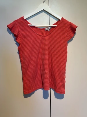 Randig röd topp från Hampton Republic - Snygg röd topp från Hampton Republic med diskreta horisontella ränder. Modellen har korta ärmar med lätt volang och v-ringad hals. Perfekt att styla med jeans eller kjol för en fräsch look.