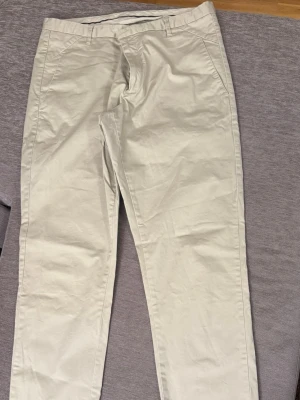 Beige chinos från Whyred - Snygga beige chinos från Whyred i klassisk rak modell. Byxorna har fickor i sidorna, bälteshällor och dragkedjegylf. Tillverkade i bomull med en mjuk och skön känsla. Perfekta för en clean och stilren look.