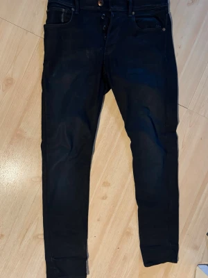 Svarta jeans från G-Star RAW - Snygga svarta jeans från G-Star RAW med klassisk femficksmodell och knappgylf. Jeansen har en strechig passform och detaljerade sömmar. Perfekta för dig som gillar en stilren och modern look. Förgen på jeansen är väldigt mörkblå. Nypris 1500 