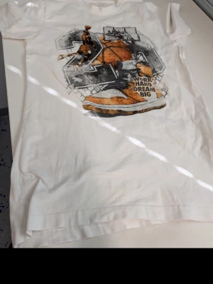 Vit t-shirt från Mixtee Tee med tryck - Vit t-shirt från Mixtee Tee med coolt grafiskt tryck framtill i svart, orange och grått. Trycket har texten 'WORK HARD DREAM BIG' och motiv av sneaker och person. Klassisk rund hals och korta ärmar. Perfekt för en avslappnad streetwear-look.