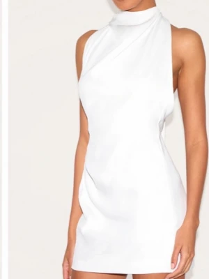 Vit kort halterneckklänning - Säljer en vit kort klänning med halterneck och öppen rygg. Klänningen har en elegant drapering vid halsen och ett långt tygstycke som faller ner baktill. Använd endast en gång så är i bra skick. Jag är 170 cm lång. Klänningen är storlek 40 och passar mig som brukar ha S/M.