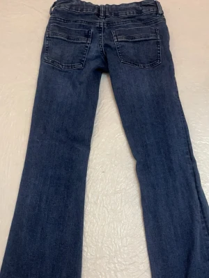 Mörkblå bootcut jeans - Säljer ett par mörkblå bootcut jeans med klassisk femficksdesign och låg midja. Jeansen har en snygg tvätt och raka ben som går ut lite nedtill. Perfekta till en avslappnad stil och passar till det mesta i garderoben.