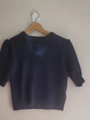 Mörkblå stickad puffärmströja - Mysig mörkblå stickad tröja med puffärmar och rund hals. Tröjan har en något kortare, boxig passform och ribbade muddar vid ärmslut och nederkant. Perfekt att styla med jeans för en avslappnad look.