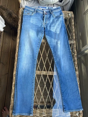 Jacob cohen jeans - Säljer ett par ljusblå jeans från jacob cohen med raka ben och klassisk femficksmodell. Jeansen har en snygg tvätt med lätt slitning och är tillverkade i bomull med lite stretch för extra komfort. Perfekta för en avslappnad och trendig look.
