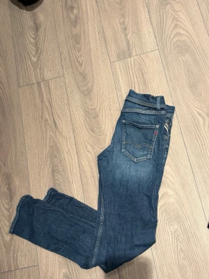 Blå jeans från Replay - Säljer ett par klassiska blå jeans från Replay med fem fickor och diskreta slitningar. Jeansen har normal midja, raka ben och är tillverkade i mjukt denimtyg. Perfekta för en avslappnad och trendig look.