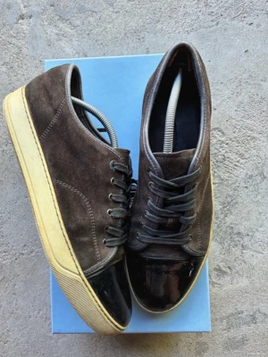 Bruna sneakers med svart lackdetalj - Bruna lanvin skor i UK9. Passar 43-44. Enda lilla skavanken är hälen på skon. Lite sliten där som man ser på sista bild. Annars bra skick. Boxen ingår. Köper man så köper man. Inga returer. 