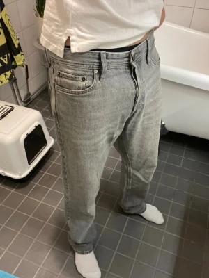 Gråa raka jeans från Jack and Jones - Säljer ett par gråa jeans från Jack and Jones  med rak passform och klassisk femficksdesign. Jeansen har en snygg tvättad look och är tillverkade i denim. Perfekta för dig som gillar en avslappnad stil. Står 30/32 men sitter mer som 32/32