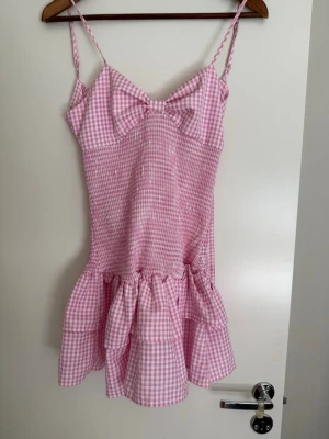 Rosa miniklänning  - Supersöt rosa och vit rutig kortklänning med volanger.  Klänningen har smala axelband och omlottknytning i ryggen. Jättefin till sommaren 🤗🤗