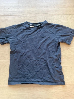 Mörkgrå t-shirt från Sail Racing - Snygg mörkgrå t-shirt från Sail Racing med diskret logga broderad på bröstet. Klassisk rund halsringning och korta ärmar. Tillverkad i mjuk bomull som känns skön mot huden. Perfekt till jeans eller shorts.