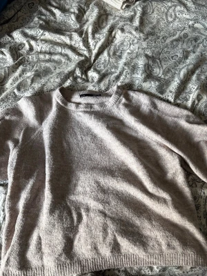 Beige stickad tröja med rund hals - Mysig beige stickad tröja med rund halsringning och avslappnad passform. Tröjan har långa ärmar och ribbade muddar vid ärmslut och nederkant. Perfekt för lager på lager och enkel att matcha med olika stilar.