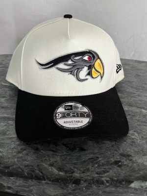 Vit och svart New Era keps 9FORTY - Snygg vit keps från New Era med svart böjd skärm och broderad fågel-logga från de mexikanska baseboll laget.  (”pueblas de perico”) i svart, grått och gult framtill. Modellen är 9FORTY och har justerbar passform. Klassisk streetwear-look med tydlig sticker på skärmen. Nypris 489 kr och kepsen är helt oanvänd. Kontakta gärna innan du köper!💛