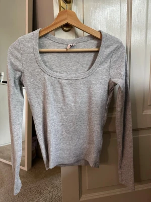 Ljusgrå ribbad topp från Nelly - Säljer en ljusgrå ribbad långärmad topp från Nelly. Toppen har en rund, djup ringning och är tillverkad i mjuk bomullsmix som sitter skönt på kroppen. Perfekt att styla med jeans eller kjol för en clean look. Den är aldrig använd och därför i nyskick.