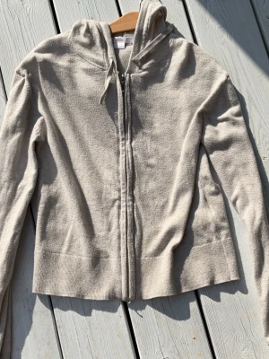 Beige  zip-hoodie med huva - En basic beige  hoodie med dragkedja och huva. Tröjan har dragsko vid huvan och är tillverkad i ett mjukt, bekvämt material. Perfekt för en avslappnad stil och enkel att matcha med andra plagg.