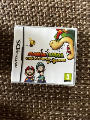 Mario & Luigi: Viaje al Centro de Bowser DS - Nintendo DS-spelet Mario & Luigi: Viaje al Centro de Bowser med färgglad omslagsbild på Mario, Luigi och Bowser. Spelet har tecknad design och plastfodral med tydlig logga och PEGI 3-märkning. Perfekt för dig som gillar äventyr och klassiska Nintendo-karaktärer.