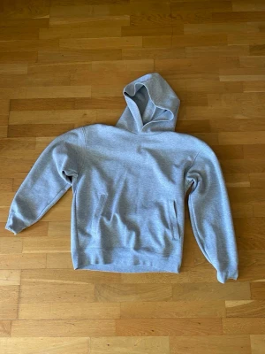 Grå uniqlo hoodie med huva - En enkel och stilren grå hoodie med huva och magficka. Hoodien har ribbade muddar vid ärmslut och nederkant. Perfekt för en avslappnad look och passar till det mesta. Materialet känns mjukt och bekvämt. 
