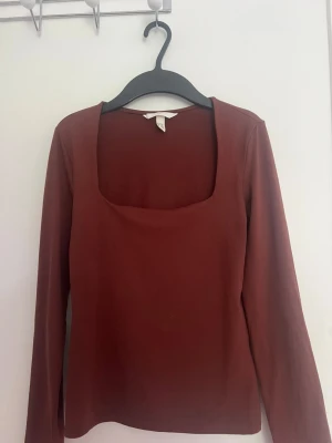 Brun långärmad topp med fyrkantig ringning - Snygg brun långärmad topp med fyrkantig ringning. Enkel och stilren design som passar perfekt till jeans eller kjol. Tillverkad i mjukt material som känns skönt mot huden. Perfekt för dig som gillar minimalistisk stil.