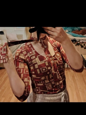 Mönstrade vintage topp med cut out❤️  - Säljer en unik topp med geometriskt mönster i vinrött, beige och brunt/orange. Toppen har trekvartsärm, cut out vid halsen och ett snyggt knytband❤️ Stretchigt material som sitter tight och ger en cool retrovibe. Real vintage! <3