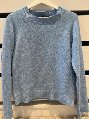 Ljusblå stickad tröja Vero Moda - Mysig ljusblå stickad tröja från Vero Moda. Tröjan har rund halsringning, långa ärmar och ribbade muddar vid ärmslut och nederkant. Perfekt för lager på lager och enkel att matcha med jeans eller kjol. Lite noprig