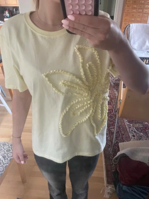 Ljusgul t-shirt med broderad blomma Zara - Supersöt ljusgul t-shirt från Zara med en stor broderad blomma framtill. T-shirten har korta ärmar och är gjord i mjuk bomull, perfekt för en chill och trendig look. Enkel att styla till både jeans och kjol.