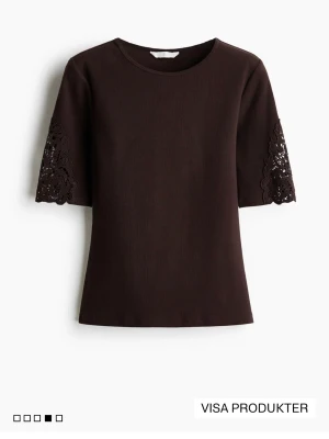 Brun topp med spetsdetaljer - Mörkbrun topp med rund hals och halvlånga ärmar. Ärmarna har snygga spetsdetaljer som ger en extra touch. Rak passform och enkel design som funkar till mycket. Perfekt för dig som gillar stilrena plagg med en twist.