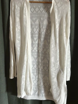 Vit stickad cardigan från Divided - Säljer en vit stickad cardigan från Divided med öppen front och snyggt geometriskt hålmönster. Lätt och luftig modell med trekvartsärmar, perfekt att slänga över en topp. Stilren och enkel att matcha till olika outfits.