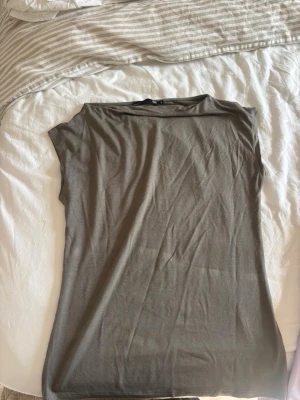Olivgrön ärmlös topp - En enkel och stilren olivgrön topp i mjukt material. Modellen är ärmlös med rak passform och rund halsringning. Perfekt att matcha med jeans eller kjol för en clean look.