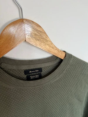 Olivgrön stickad tröja Massimo Dutti - Snygg olivgrön stickad tröja från Massimo Dutti med rund halsringning och diskret strukturmönster. Tröjan har långa ärmar och ribbade muddar vid ärmslut och nederkant. Perfekt till lager på lager och enkel att matcha. Storlek S. Mycket fint skick