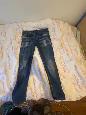 Blå slitna jeans från Dsquared2 - Säljer ett par blå jeans från Dsquared2 med slitningar och tvättade detaljer. Jeansen har klassisk femficksmodell, normal midja och raka ben. Materialet är denim i bomull och de har en cool, avslappnad look. Knappt använda men storlek 32