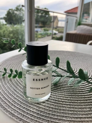 Essnce Hotter Mimosa parfym - Fräsch parfym från Essnce med doften Hotter Mimosa. Flaskan är cylindrisk i genomskinligt glas med svart rund kork och enkel vit etikett. Modern och stilren design som passar perfekt på sminkbordet. Eau de Parfum-variant.