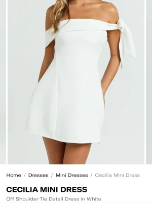 Oanvänd Vit offshoulder miniklänning  - Oanvänd klänning med prislapp på! Stilren vit miniklänning med offshoulder-design och en stor rosett på ena axeln. Klänningen har en figurnära passform och är perfekt för dig som vill ha en enkel men elegant look. Tillverkad i ett mjukt och följsamt material.