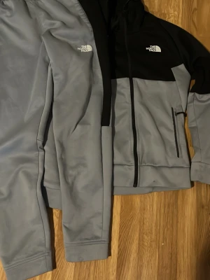 Gråa mjukisbyxor från The North Face - Säljer ett par gråa mjukisbyxor från The North Face med vit logga på låret. Byxorna har en avslappnad passform och resår i midjan samt vid bensluten. Perfekta för chill dagar eller när du vill vara bekväm. Matcha gärna med hoodie för en komplett look.