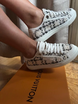 Louis Vuitton liknande tweed sneakers vita/svarta - Snygga Louis Vuitton liknande sneakers i vit och blå tweed med vita läderdetaljer och klassisk logotyp på sidan. Skorna har vita snören och en låg silhuett som ger en clean och trendig look. Perfekta för dig som vill sticka ut med exklusiva detaljer och unik textur. små 38:or, använda på endast en promenad. skambud undanbedes 