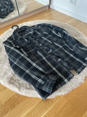 Svartvitrutig overshirt från  - Overshirt i svart och vitt rutmönster från H&M. Klassisk krage, knäppning framtill och två bröstfickor med lock. Tjockare material som ger en schysst lager-på-lager-look. Perfekt till jeans eller cargobyxor.