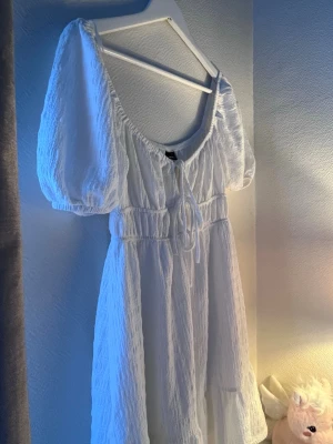 Klänning  - Söt vit kort klänning med puffärmar och knyt i midjan. Klänningen har en lätt strukturerad yta och volang nedtill. Perfekt för sommarens alla tillfällen och ger en romantisk vibe.