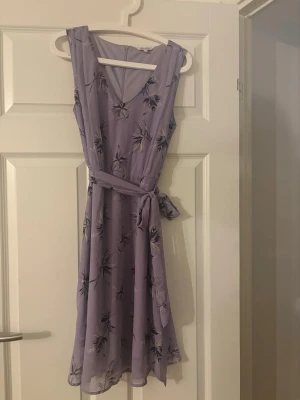 Ljuslila blommig klänning Alice Bizous - Söt ljuslila klänning från Alice Bizous med blommigt mönster och knytband i midjan. Säljs pga den inte kommer till använding.
