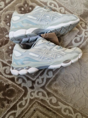 Asics vita och ljusgrå sneakers - Snygga sneakers från Asics i vitt och ljusgrått med mesh- och syntetpaneler. Skorna har klassisk Asics-logga på sidan, vadderad plös och krage samt en chunky sula med silverdetaljer. Perfekta för dig som gillar sportig och clean stil.