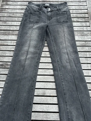 Grå utsvängda jeans från Madlady - Säljer ett par grå jeans från Madlady med utsvängda ben och markerade sömmar framtill. Jeansen har två stora fickor fram och dubbla knappar i midjan. Fickorna bak har en fin design och passar perfekt för dig som söker en stockholmsk look😍